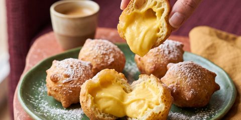 Buñuelos de viento dorados espolvoreados con azúcar glas, rellenos de crema pastelera de azafrán Antonio Sotos y chocolate blanco.